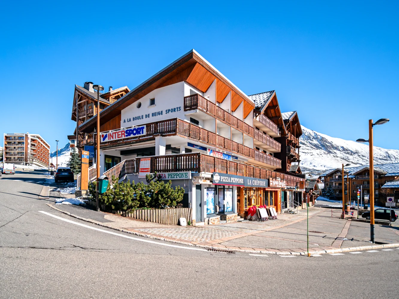 Le site du projet La Cristallière à l’Alpe d’Huez avant les travaux : le bâtiment existant et ses commerces, à l’angle de la rue